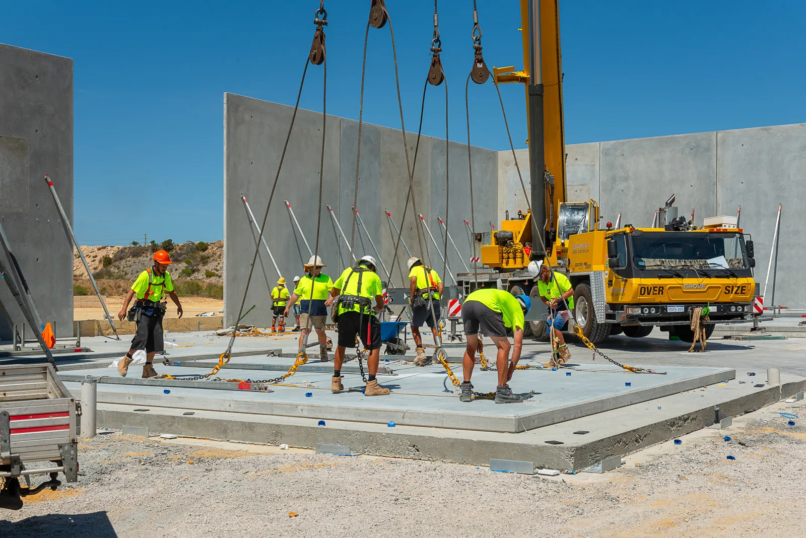 people in safety gear rigging up a concrete panel to be erected by a crane